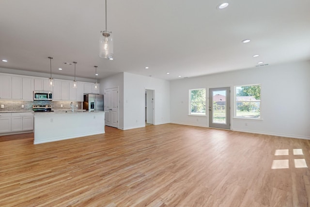 kitchen featuring white cabinetry, a center island with sink, pendant lighting, stainless steel appliances, and decorative backsplash