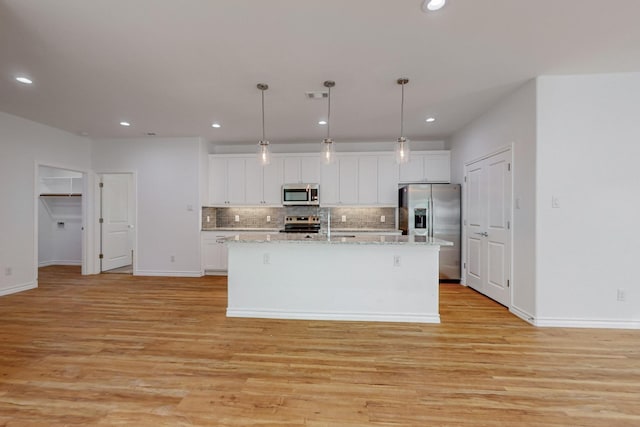 kitchen featuring appliances with stainless steel finishes, hanging light fixtures, a center island with sink, and white cabinets