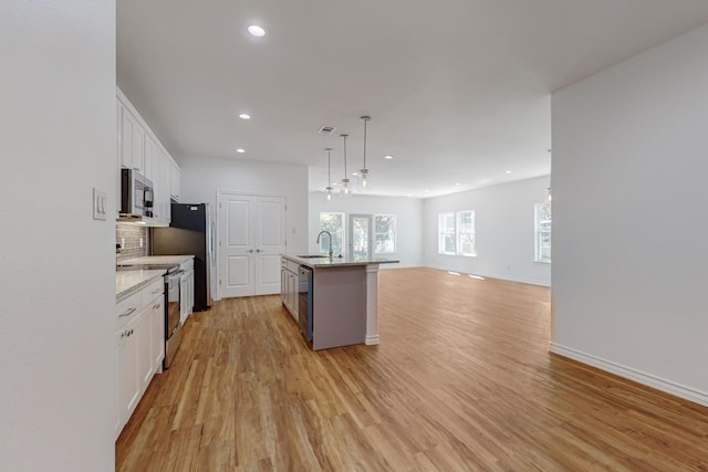 kitchen with sink, hanging light fixtures, stainless steel appliances, an island with sink, and white cabinets