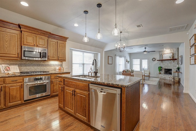 kitchen featuring pendant lighting, an island with sink, sink, stainless steel appliances, and light stone countertops