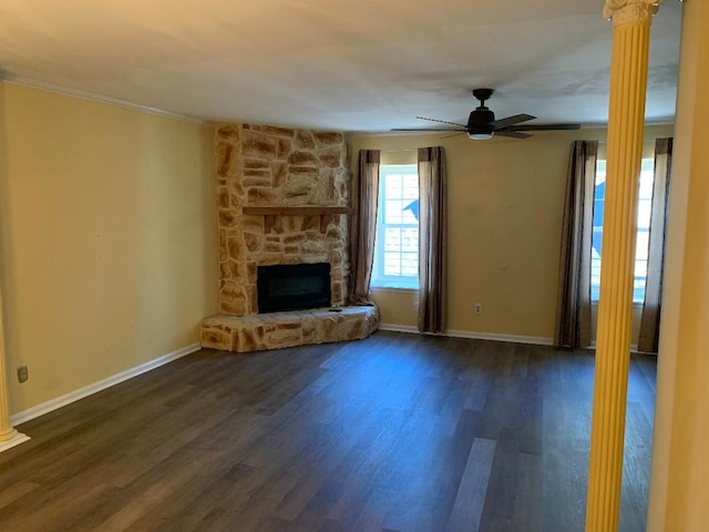 unfurnished living room with decorative columns, a stone fireplace, dark wood-type flooring, and ceiling fan