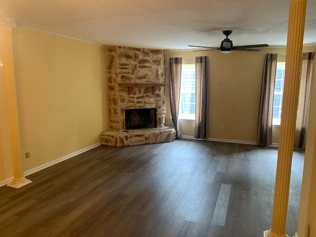 unfurnished living room with crown molding, dark wood-style flooring, a fireplace, a ceiling fan, and ornate columns