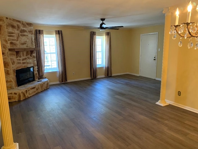 unfurnished living room featuring a stone fireplace, a healthy amount of sunlight, ceiling fan with notable chandelier, and dark hardwood / wood-style flooring