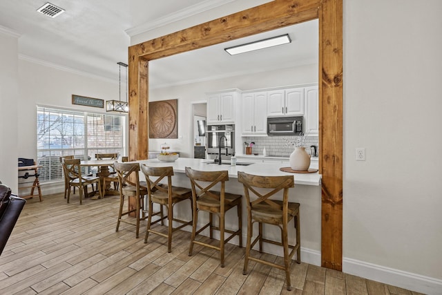 kitchen featuring sink, light hardwood / wood-style flooring, crown molding, decorative backsplash, and white cabinets