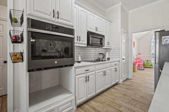 kitchen with tasteful backsplash, crown molding, white cabinets, black appliances, and light wood-type flooring