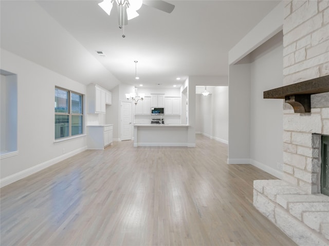 unfurnished living room with light wood-type flooring, a large fireplace, vaulted ceiling, and ceiling fan with notable chandelier