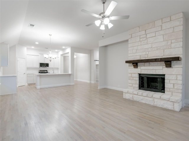 unfurnished living room with vaulted ceiling, a fireplace, ceiling fan with notable chandelier, and light hardwood / wood-style floors