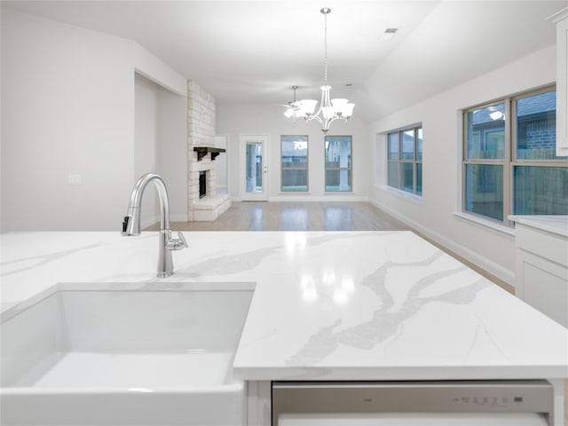 kitchen with light stone countertops, decorative light fixtures, a stone fireplace, sink, and white dishwasher