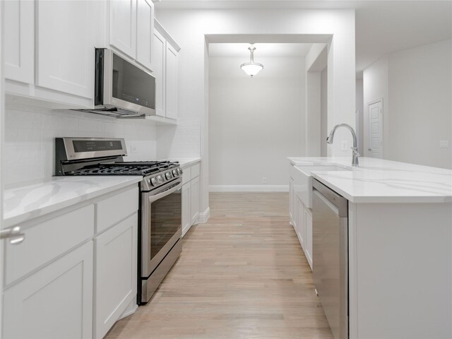 kitchen with pendant lighting, white cabinetry, a kitchen island with sink, light stone countertops, and stainless steel appliances