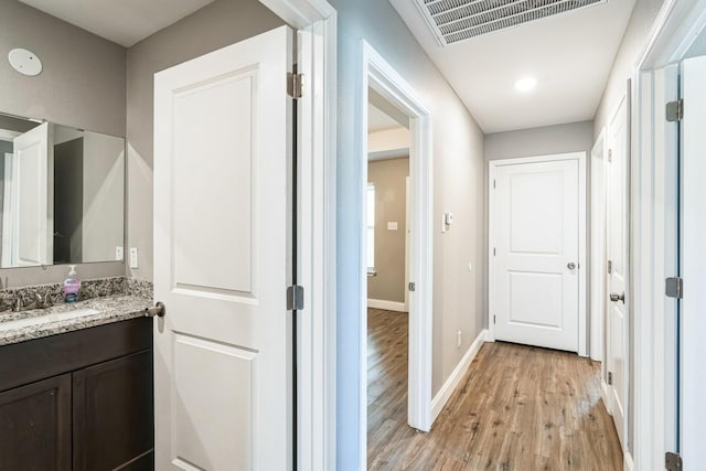 corridor with light wood-type flooring and sink