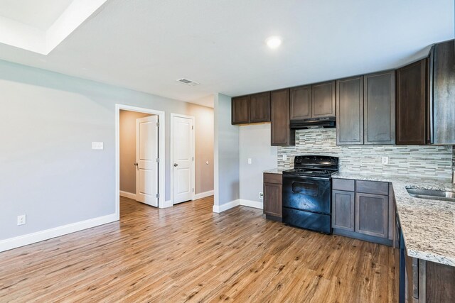 kitchen featuring dark brown cabinetry, light stone countertops, tasteful backsplash, black electric range, and light wood-type flooring