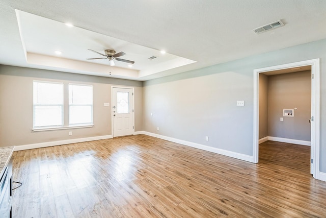 interior space with light wood-type flooring, a raised ceiling, and ceiling fan