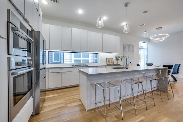 kitchen with white cabinetry, sink, hanging light fixtures, oven, and an island with sink