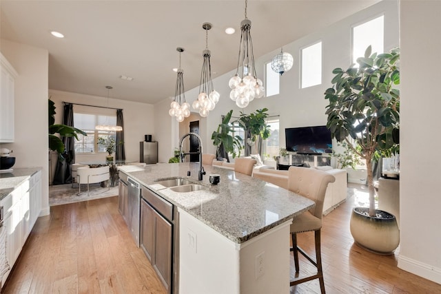 kitchen featuring light stone countertops, stainless steel dishwasher, sink, a center island with sink, and white cabinetry