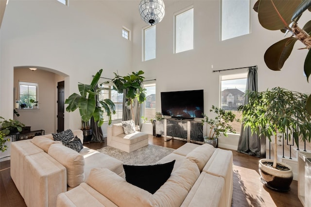 living room featuring a healthy amount of sunlight, a towering ceiling, and dark wood-type flooring