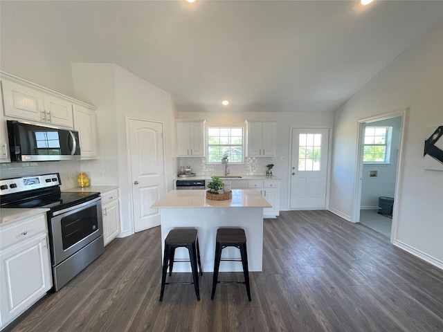 kitchen with lofted ceiling, sink, white cabinetry, stainless steel appliances, and a center island