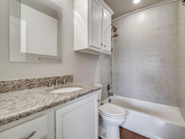 full bathroom featuring hardwood / wood-style flooring, vanity, tiled shower / bath combo, and toilet