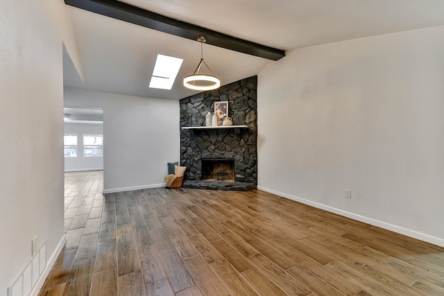 unfurnished living room with hardwood / wood-style flooring, a stone fireplace, and vaulted ceiling with skylight