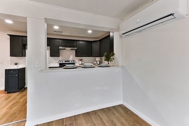 kitchen with electric range, kitchen peninsula, and a wall mounted AC