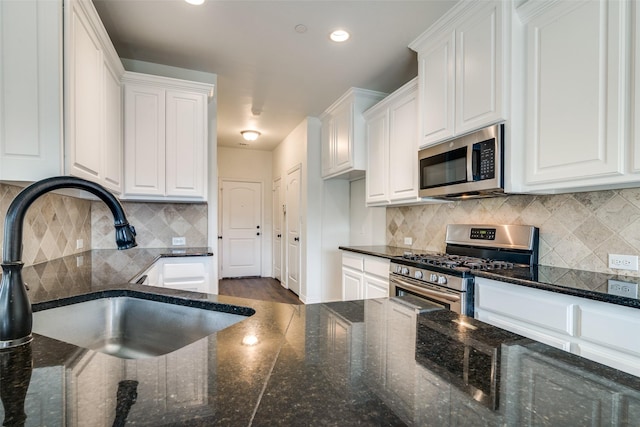 kitchen featuring white cabinets, appliances with stainless steel finishes, dark stone counters, and sink