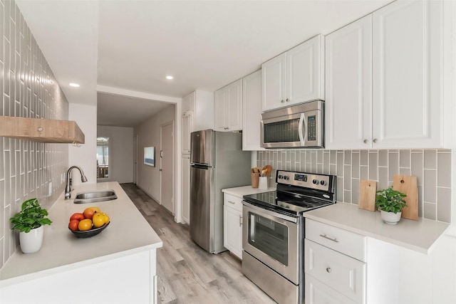 kitchen with white cabinets, sink, appliances with stainless steel finishes, and light hardwood / wood-style flooring