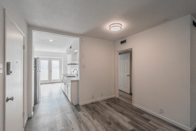 corridor with a textured ceiling, dark hardwood / wood-style floors, sink, and french doors