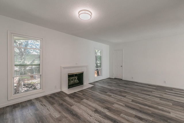 unfurnished living room with plenty of natural light, dark wood-type flooring, and a tiled fireplace