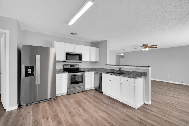 kitchen with kitchen peninsula, appliances with stainless steel finishes, a textured ceiling, sink, and white cabinetry