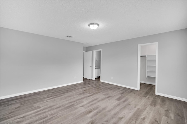 unfurnished bedroom featuring light hardwood / wood-style floors, a walk in closet, a textured ceiling, and a closet