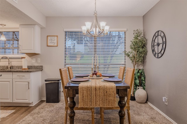 dining space with sink, light hardwood / wood-style floors, a textured ceiling, and an inviting chandelier