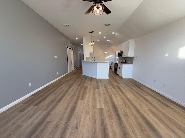 unfurnished living room featuring ceiling fan, sink, a barn door, vaulted ceiling, and hardwood / wood-style flooring