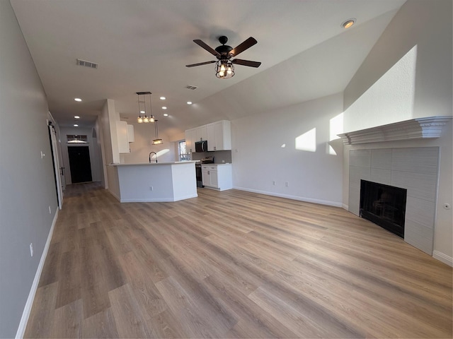 unfurnished living room featuring sink, vaulted ceiling, ceiling fan, a fireplace, and light hardwood / wood-style floors