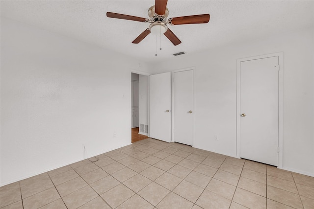 unfurnished bedroom with light tile patterned floors, a textured ceiling, and ceiling fan