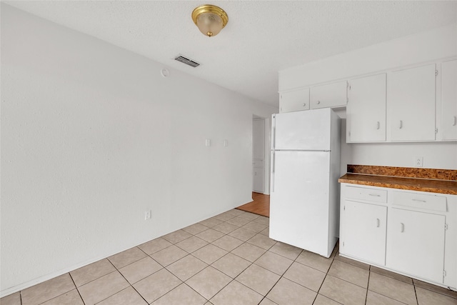 kitchen with white cabinets, light tile patterned flooring, a textured ceiling, and white refrigerator