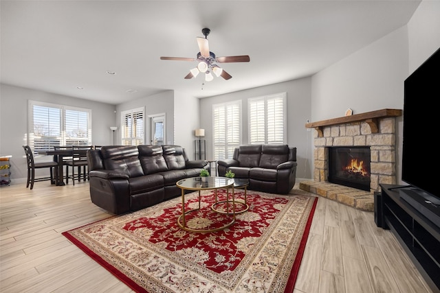 living room with a stone fireplace, ceiling fan, and light wood-type flooring