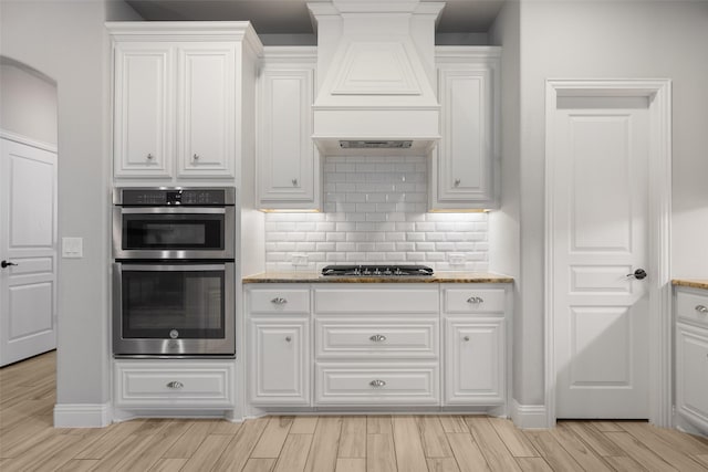 kitchen with premium range hood, light stone counters, white cabinets, and stainless steel appliances