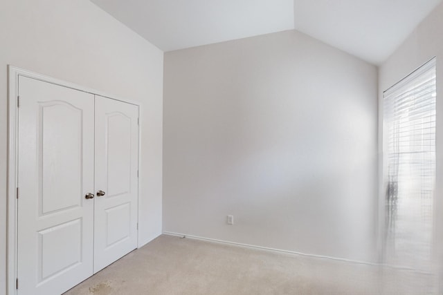 unfurnished bedroom featuring light carpet, a closet, and lofted ceiling