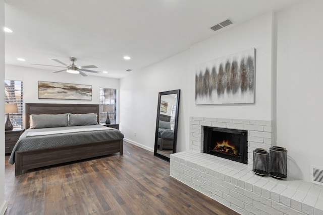 bedroom featuring a brick fireplace, dark hardwood / wood-style floors, and ceiling fan