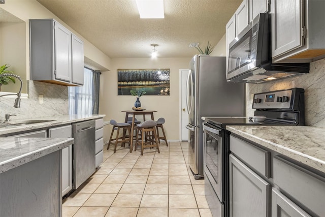 kitchen featuring appliances with stainless steel finishes, a textured ceiling, light tile patterned floors, and gray cabinetry