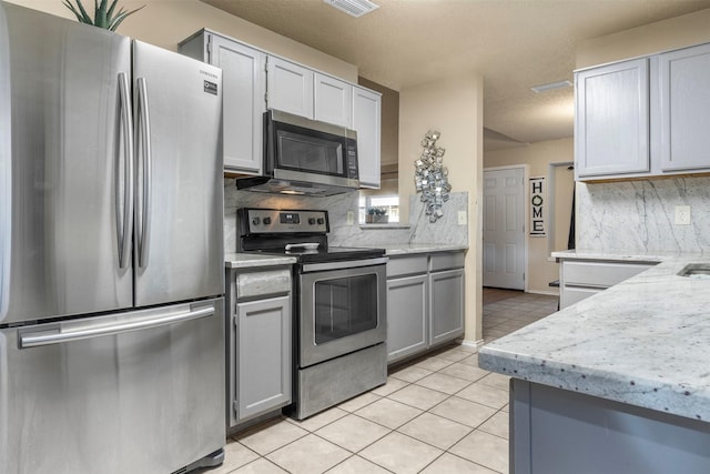 kitchen featuring light tile patterned floors, stainless steel appliances, gray cabinets, and tasteful backsplash