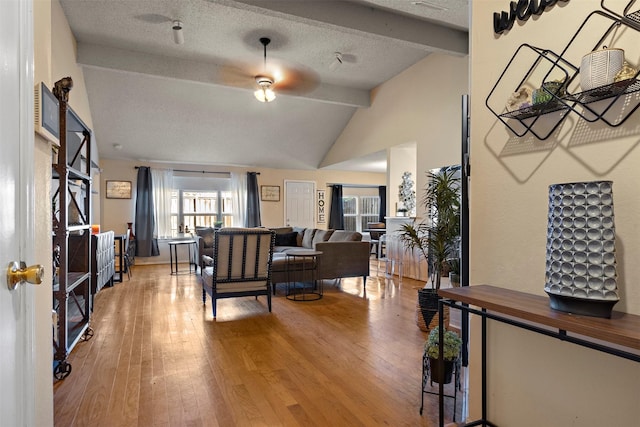 living room featuring light wood-type flooring, a textured ceiling, lofted ceiling with beams, and ceiling fan