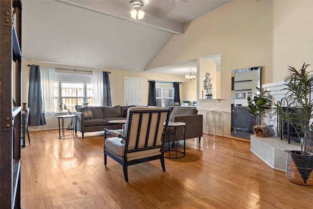 living room featuring lofted ceiling with beams, ceiling fan with notable chandelier, and light hardwood / wood-style flooring