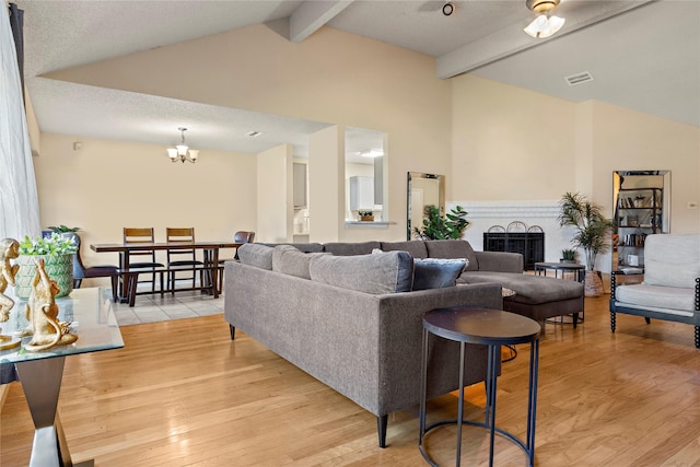 living room with a textured ceiling, lofted ceiling with beams, light hardwood / wood-style flooring, and an inviting chandelier