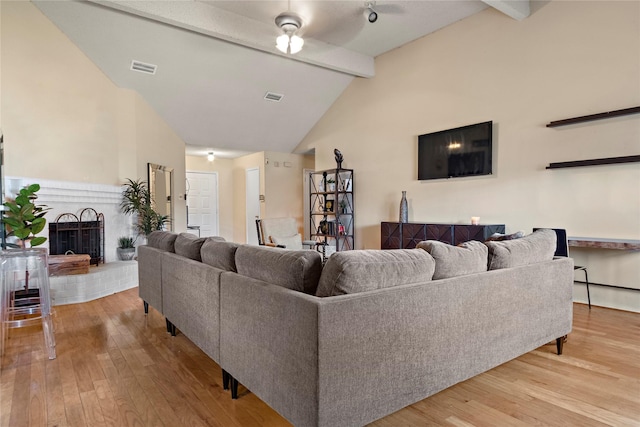 living room featuring a brick fireplace, lofted ceiling with beams, ceiling fan, and light hardwood / wood-style flooring