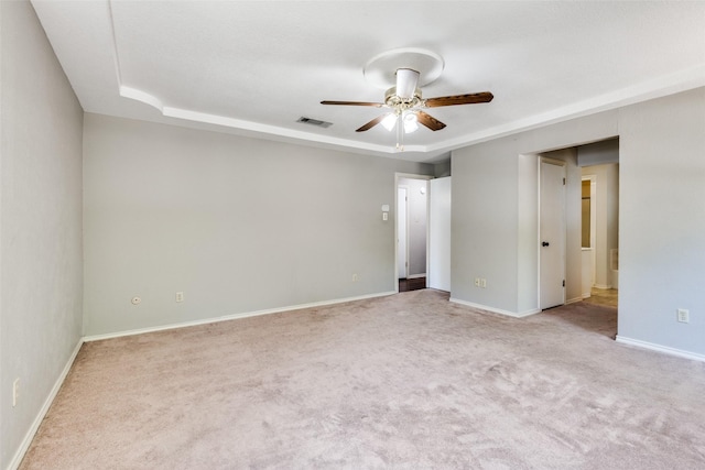 unfurnished room featuring a raised ceiling, light colored carpet, and ceiling fan