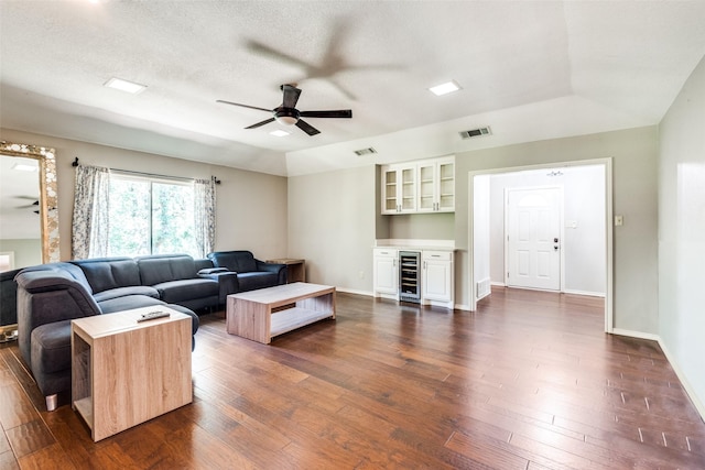 living room featuring ceiling fan, dark hardwood / wood-style floors, a textured ceiling, bar area, and beverage cooler