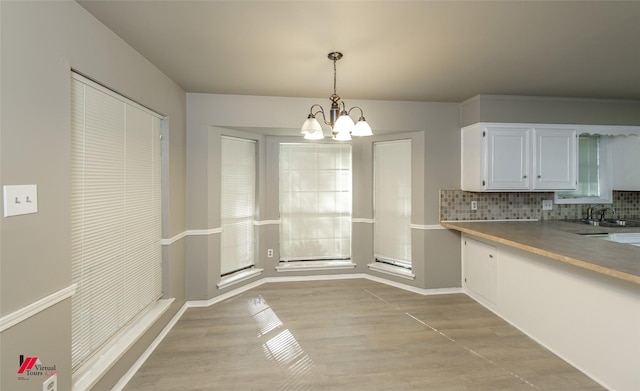 kitchen with white cabinetry, backsplash, decorative light fixtures, and light hardwood / wood-style floors