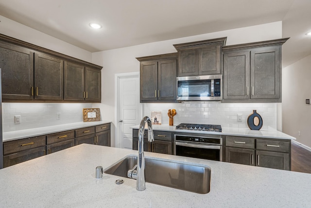 kitchen featuring sink, backsplash, light stone countertops, and appliances with stainless steel finishes