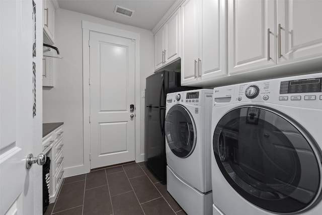 clothes washing area featuring cabinets, dark tile patterned floors, and washer and clothes dryer