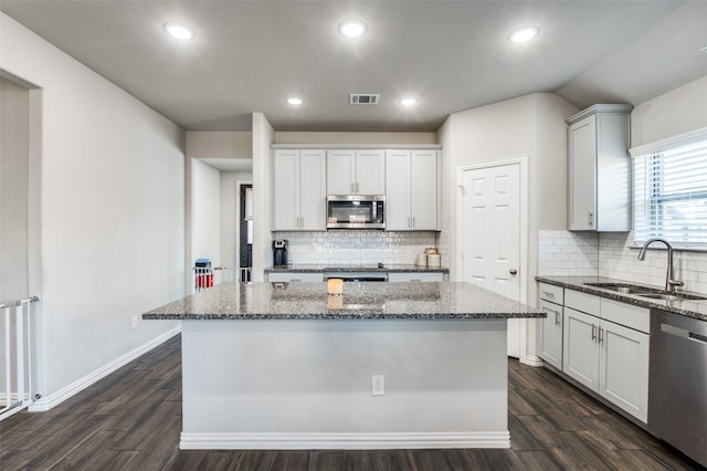 kitchen with sink, stainless steel appliances, dark hardwood / wood-style floors, a center island, and dark stone counters